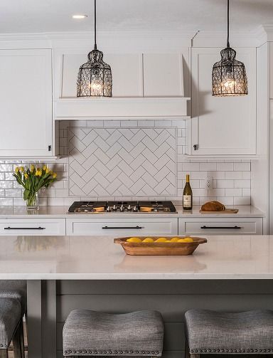 Bright white modern kitchen with herringbone backsplash, pendant lights, and a fruit bowl on the island