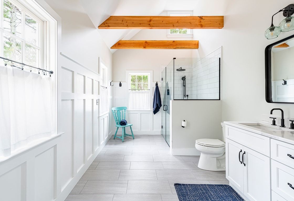 Bright white modern bathroom with wood beams, vanity, toilet, and small teal stool in a hallway-like space