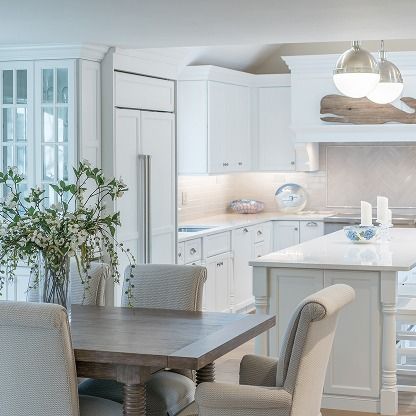 Bright white kitchen and dining area with island, table, pendant lights, and a potted plant