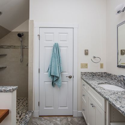 Bright bathroom with white door, teal towel, granite vanity, and glass shower stall