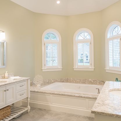 Elegant bathroom with a white soaking tub, double vanity, marble counters, and three arched windows