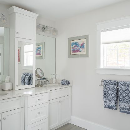 Bright white bathroom vanity with mirror, blue patterned towels, framed art, and a window with blinds