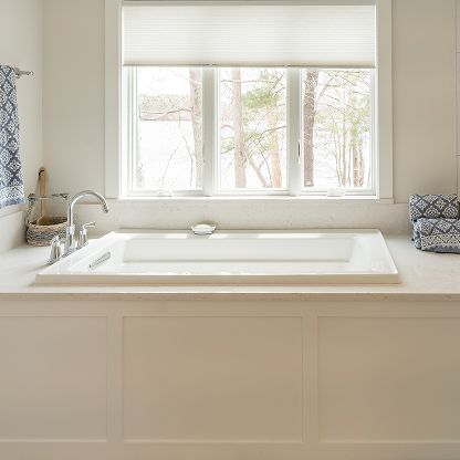 Bright bathroom with a white soaking tub beneath a window and light beige cabinetry