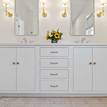 Bright white bathroom vanity with gold fixtures, mirrors, and a vase of sunflowers on the counter
