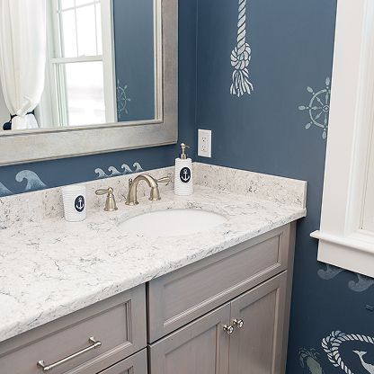 Bathroom vanity with white marble countertop, brass faucet, and blue walls with white decor accents