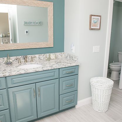 Light blue bathroom vanity with marble countertop, large mirror, and white woven laundry basket on the floor.