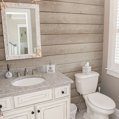 Bright bathroom with white vanity, sink, mirror, and toilet beside a window on beige shiplap walls