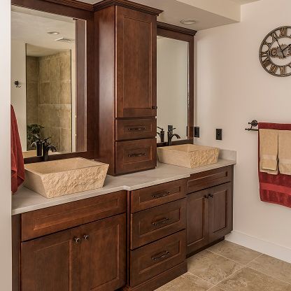 Bathroom vanity with dark wood cabinets, double sinks, and mirrored storage cabinet under warm lighting