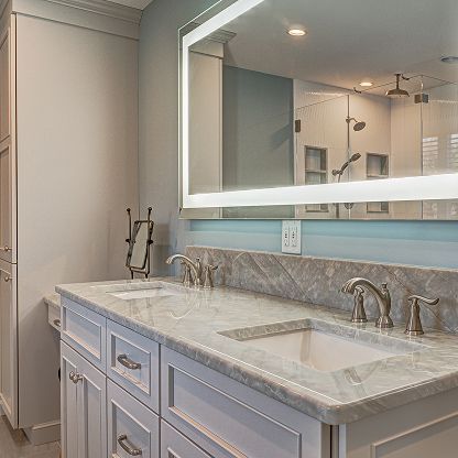 Modern bathroom vanity with marble countertop, double sink, large mirror, and glass shower in the background