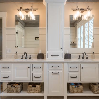 Double vanity bathroom with white cabinets, large mirrors, chrome faucets, and wicker baskets below.