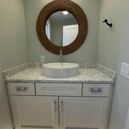 Small bathroom vanity with round mirror, granite countertop, and gray sink.