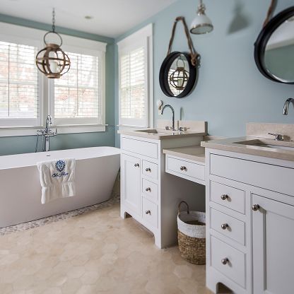Bright bathroom with white vanity, freestanding tub, round mirrors, and pale blue walls