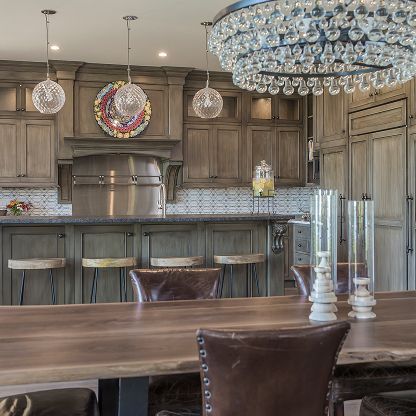 Elegant kitchen with wood cabinetry, marble island, and a large crystal chandelier over a dining table.