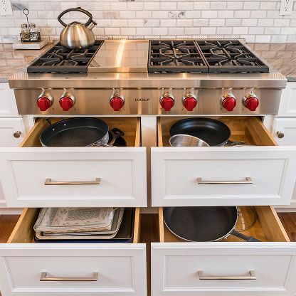 Built-in stainless-steel stovetop with red knobs above open drawers holding pots and pans