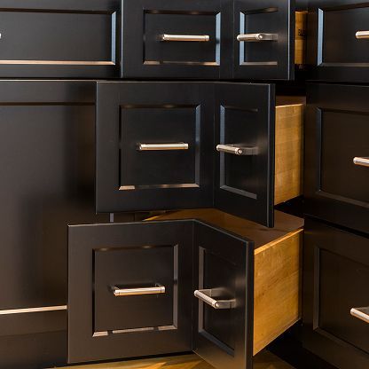 Open kitchen cabinet drawers and doors in dark wood with chrome handles, showing empty wooden interiors.
