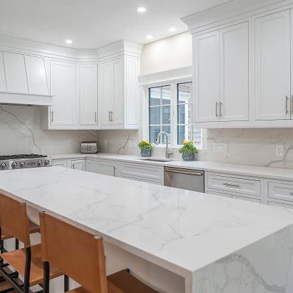 Bright white modern kitchen with marble island, white cabinets, stainless appliances, and wooden stools