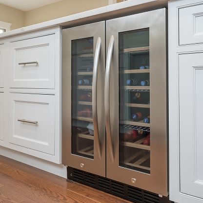 Built-in stainless steel wine cooler between white kitchen cabinets on a hardwood floor