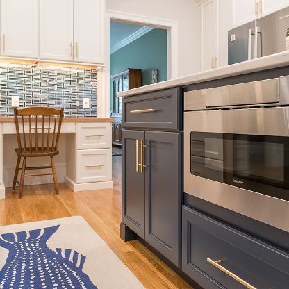 Modern kitchen with white cabinets, blue island drawers, stainless oven, and patterned rug