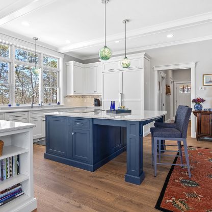 Bright kitchen with navy island, white cabinets, wood floors, and large windows
