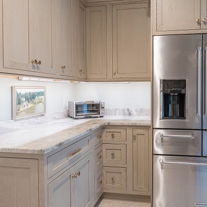 Bright kitchen with beige cabinets, marble countertops, and stainless steel refrigerator and toaster oven