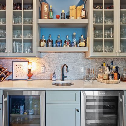 Modern kitchen with glass-front cabinets, blue decor, sink, and undercounter wine cooler and fridge.