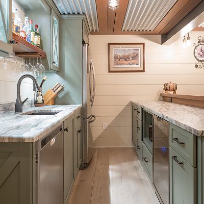 Narrow galley kitchen with marble counters, mint cabinets, sink, and wood ceiling panels