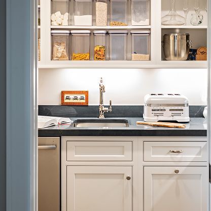 Bright kitchen sink with chrome faucet, white cabinets, open shelves, and a toaster on the counter
