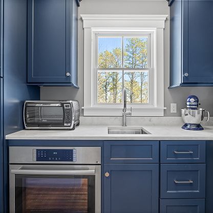Blue kitchen with white window, stainless oven, countertop toaster oven, sink, and stand mixer