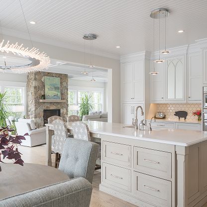 Bright white open-plan kitchen and living room with island, dining chairs, fireplace, and large windows