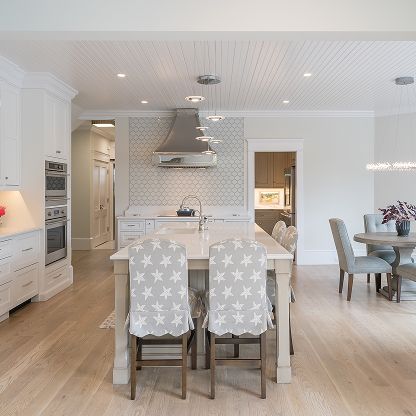 Bright modern kitchen and dining area with white cabinets, light wood floors, and star-patterned chairs