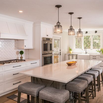 Bright white modern kitchen with a large island, gray stools, and pendant lights, seen in daylight