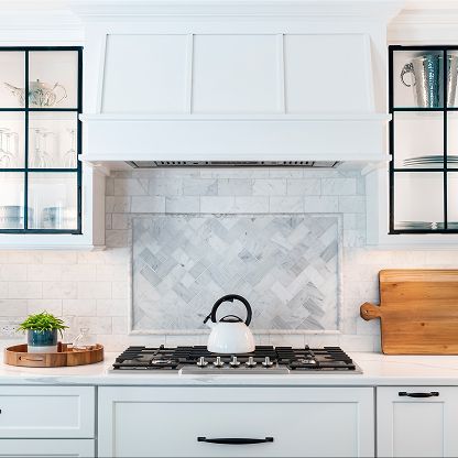 Bright white kitchen with black window frames, marble backsplash, gas range, and wooden cutting board