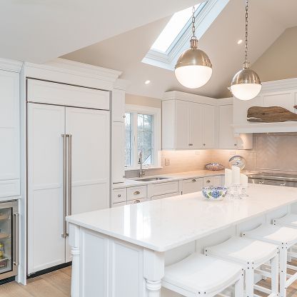 Bright white kitchen with island, bar stools, skylights, and stainless-steel refrigerator