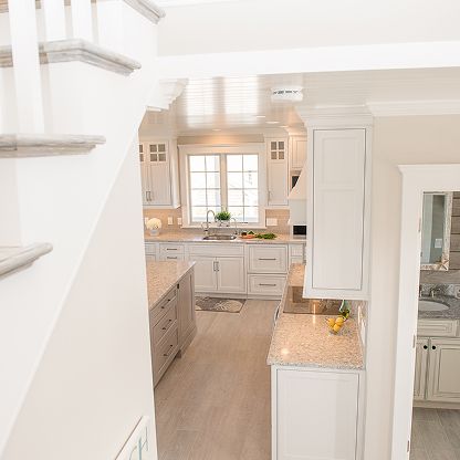 Bright white kitchen with island, farmhouse sink by window, and light wood floors