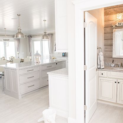 Bright white bathroom with double vanity, large mirrors, pendant lights, and open doorway to a shower area