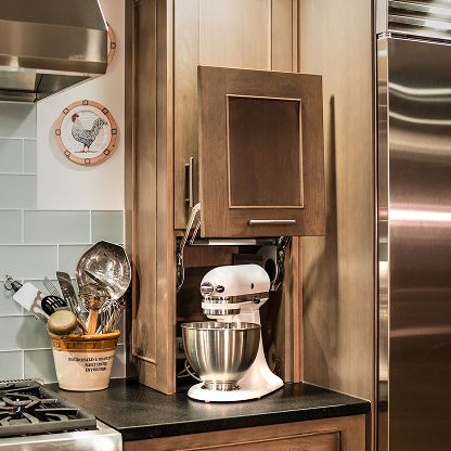Kitchen counter with a white stand mixer under wooden cabinets beside a utensil crock and stove.