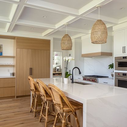 Bright modern kitchen with white island, wicker stools, wood cabinets, and woven pendant lights