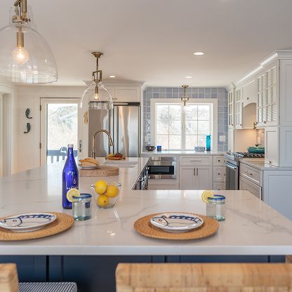 Bright white modern kitchen with a blue island, pendant lights, and a window over the sink