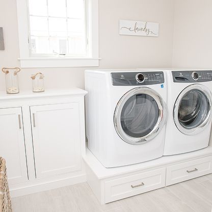 Bright laundry room with white washer and dryer, built-in cabinets, and a window