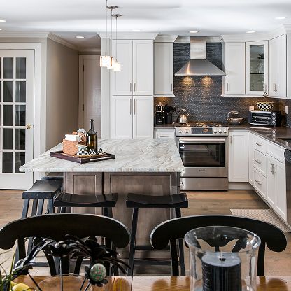 Modern white kitchen with marble island, stainless steel appliances, and pendant lights