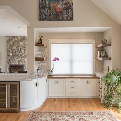 Bright living room with white cabinets, wood floors, large window, and stone fireplace niche
