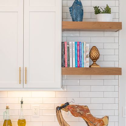 Modern kitchen wall with white cabinets, open wood shelves, books, decor, and a white subway tile backsplash