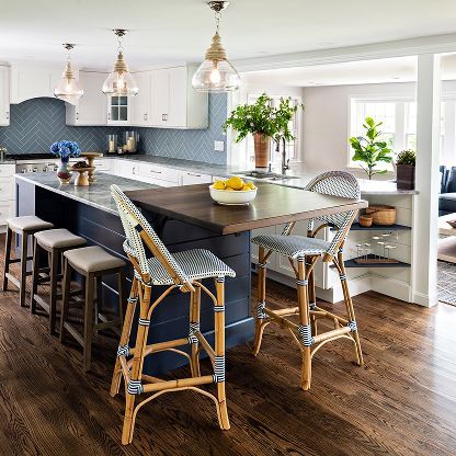 Modern kitchen with dark island, wicker bar stools, white cabinets, and bright windows