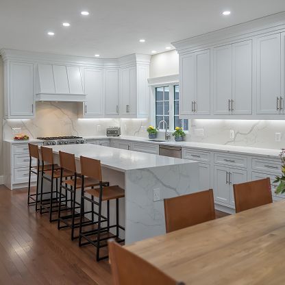 Bright modern white kitchen with marble island, wood bar stools, and recessed lighting