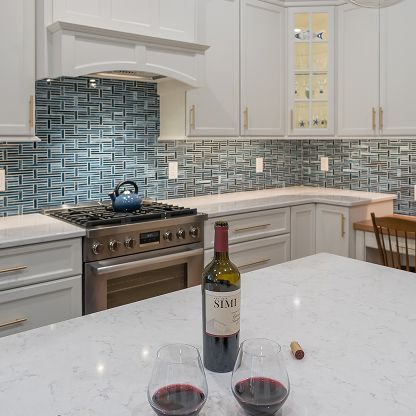 White kitchen with blue tile backsplash, stove, and wine bottle with two glasses on the counter.