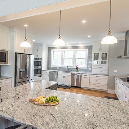 Bright modern kitchen with granite island, stainless appliances, white cabinets, and pendant lights.
