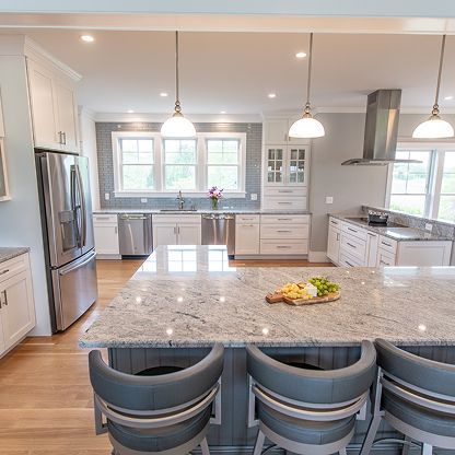 Bright modern kitchen with large island, pendant lights, stainless appliances, and gray barstools