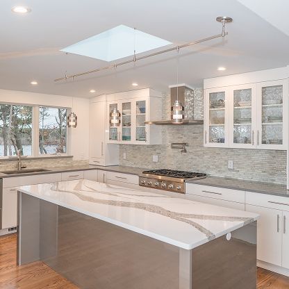 Bright modern kitchen with white cabinets, marble island, skylight, and stainless steel range hood