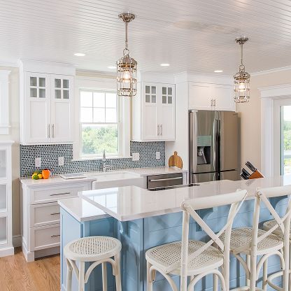 Bright white kitchen with island, pendant lights, stainless steel fridge, and blue accents