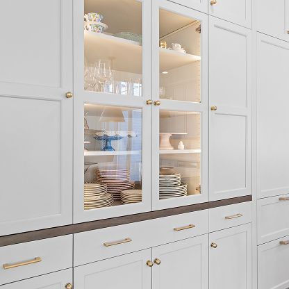 White kitchen cabinets with glass doors displaying dishes and glassware, accented by gold handles.